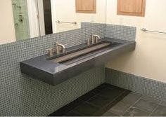 a bathroom sink sitting under a mirror next to a tiled wall and two sinks in front of it