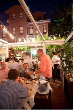 a group of people sitting around a table at a restaurant eating food and drinking wine