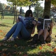 two women sitting under a tree reading books in the fall or early afternoon time,