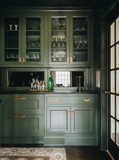 a kitchen with green cabinetry and glassware on the counter top, along with an area rug