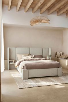 a large bed sitting under a wooden ceiling next to a white chair and ottoman on top of a rug