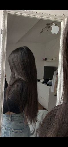 a woman standing in front of a mirror looking at her hair and wearing a white t - shirt