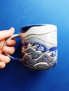 a hand holding a blue and white coffee cup with waves on it's side