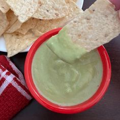 a person dipping tortilla chips into a bowl with guacamole in it