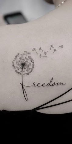 a woman's shoulder with a dandelion tattoo that reads, i am freedom