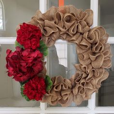 a burlock wreath with pink and red flowers hanging on a window sill