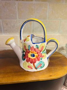 a tea pot with a flower painted on it sitting on top of a wooden table