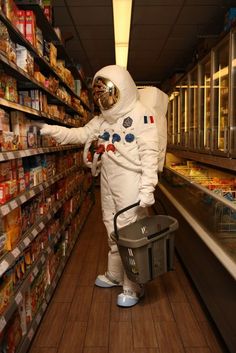 a man in an astronaut suit is picking out canned food from the shelves at a grocery store