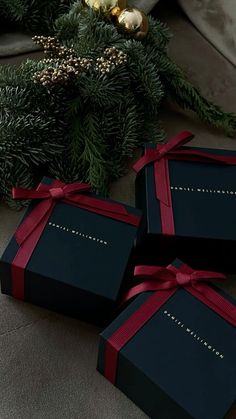 three black boxes with red bows on them sitting next to christmas decorations and greenery