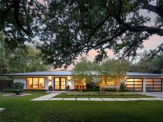 a modern house is lit up at night in the evening with trees and grass surrounding it