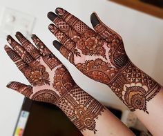 two hands with henna designs on them, one is showing off the intricate design