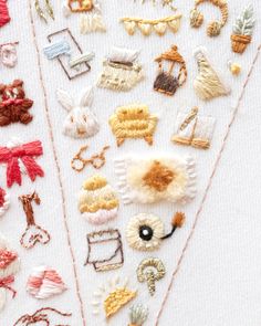 several different types of embroidered objects on a white tablecloth with red and yellow thread