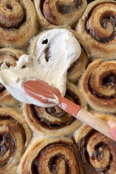 someone is painting the cinnamon rolls with white icing