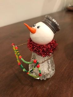 a glass snowman with an orange nose and hat on top of a wooden table