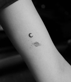 a black and white photo of a small saturn tattoo on the left inner arm,