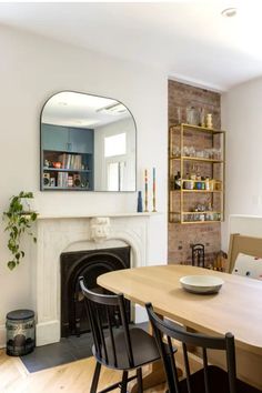 a dining room table with chairs and a fire place in front of a mirror on the wall