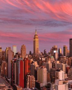 the city skyline is lit up at sunset with pink clouds in the sky above it