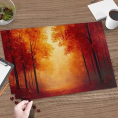 a person is painting an autumn scene on a wooden table with a cup of coffee