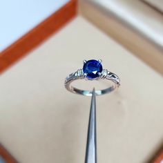 a blue ring sitting on top of a piece of jewelry in a box with a needle