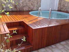 a hot tub sitting on top of a wooden deck next to a stone wall and stairs