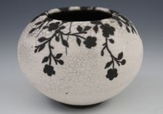 a black and white vase with flowers painted on the outside, sitting on a gray surface