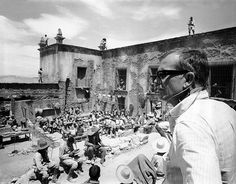 a man standing in front of an old building talking on a cell phone while surrounded by people