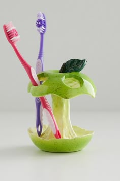 three toothbrushes are placed in an apple shaped bowl with leaves on the top