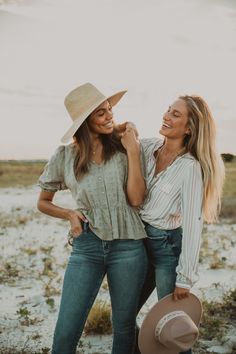 two women standing next to each other in the sand with hats on their heads and smiling