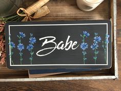 there is a sign that says babe on it and blue flowers in the bottom right corner