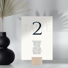 the table numbers are placed next to a black vase with a palm leaf in it