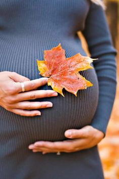 a pregnant woman's belly with a leaf in her hand, against a backdrop of autumn leaves