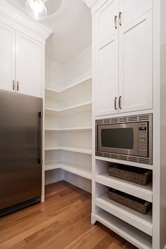 an empty kitchen with white cabinets and stainless steel appliances, including a microwave on the wall