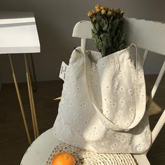 a white bag sitting on top of a chair next to an orange and a flower