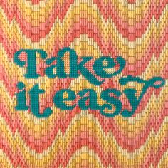 the words take it easy are painted on a piece of woven material that is pink, yellow and green