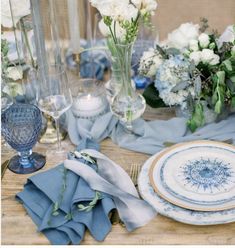 the table is set with blue and white plates, napkins, silverware, and flowers