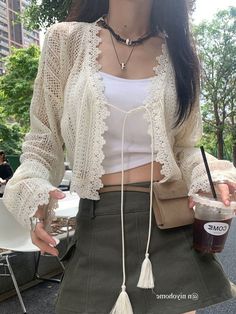 a woman wearing a white top and green skirt holding a drink in her hand while standing on the street