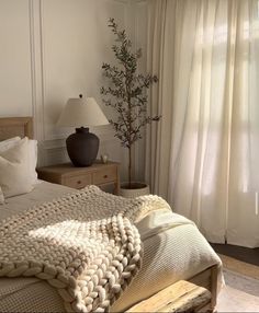 a bed sitting next to a window covered in white blankets and pillows on top of a wooden frame