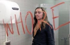 a woman standing in front of a urinal with graffiti on the wall behind her