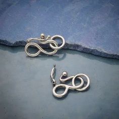 two pairs of earrings sitting on top of a blue cloth next to a pair of scissors