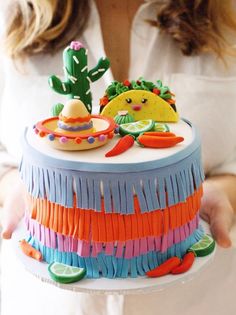 a woman holding a cake decorated with tacos and sombreros on it's sides