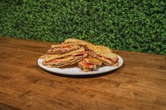 a sandwich cut in half sitting on top of a white plate next to a green hedge