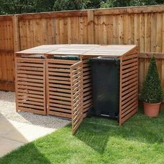 a wooden fence next to a black trash can and potted plant in the yard