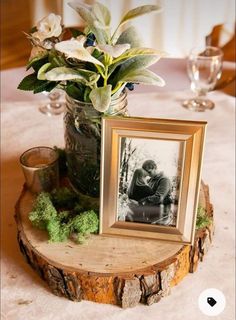 a vase with flowers and an old photo is on a tree stump at the table