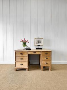 an old wooden desk with two drawers and flowers on it in front of a white wall