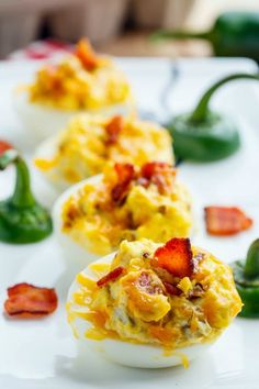 deviled eggs stuffed with bacon and cheese on a white plate next to green peppers