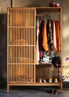 an open wooden cabinet with clothes hanging on the rack and shoes sitting on the floor