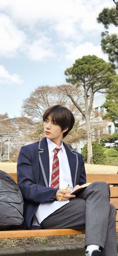 a man sitting on top of a wooden bench wearing a suit and holding a pen