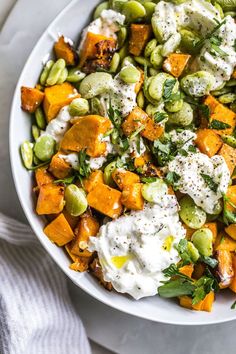 a white bowl filled with vegetables on top of a table next to a fork and napkin