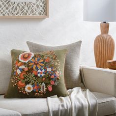 a couch with a pillow on it next to a lamp and vase in the corner