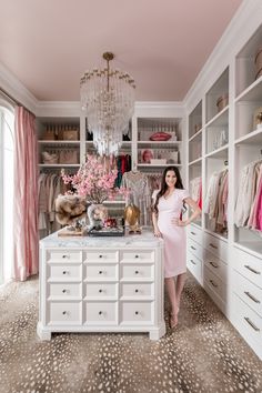 a woman standing in front of a closet filled with white drawers and pink curtains on the walls